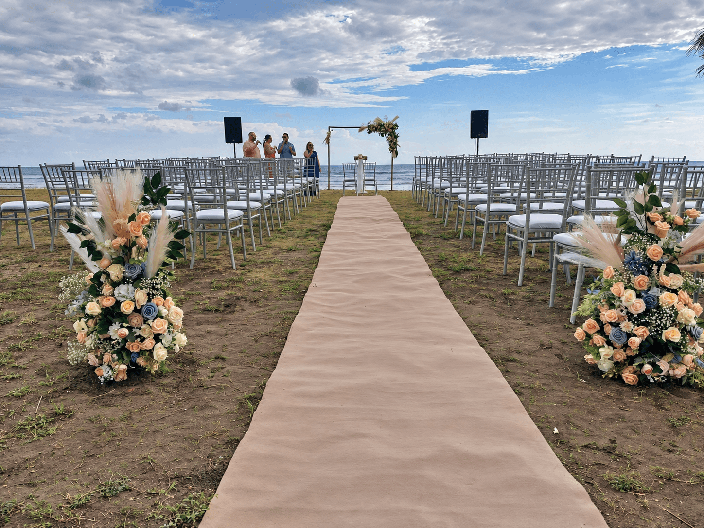 Pasillo y sillas con arreglos florales para una ceremonia en la playa