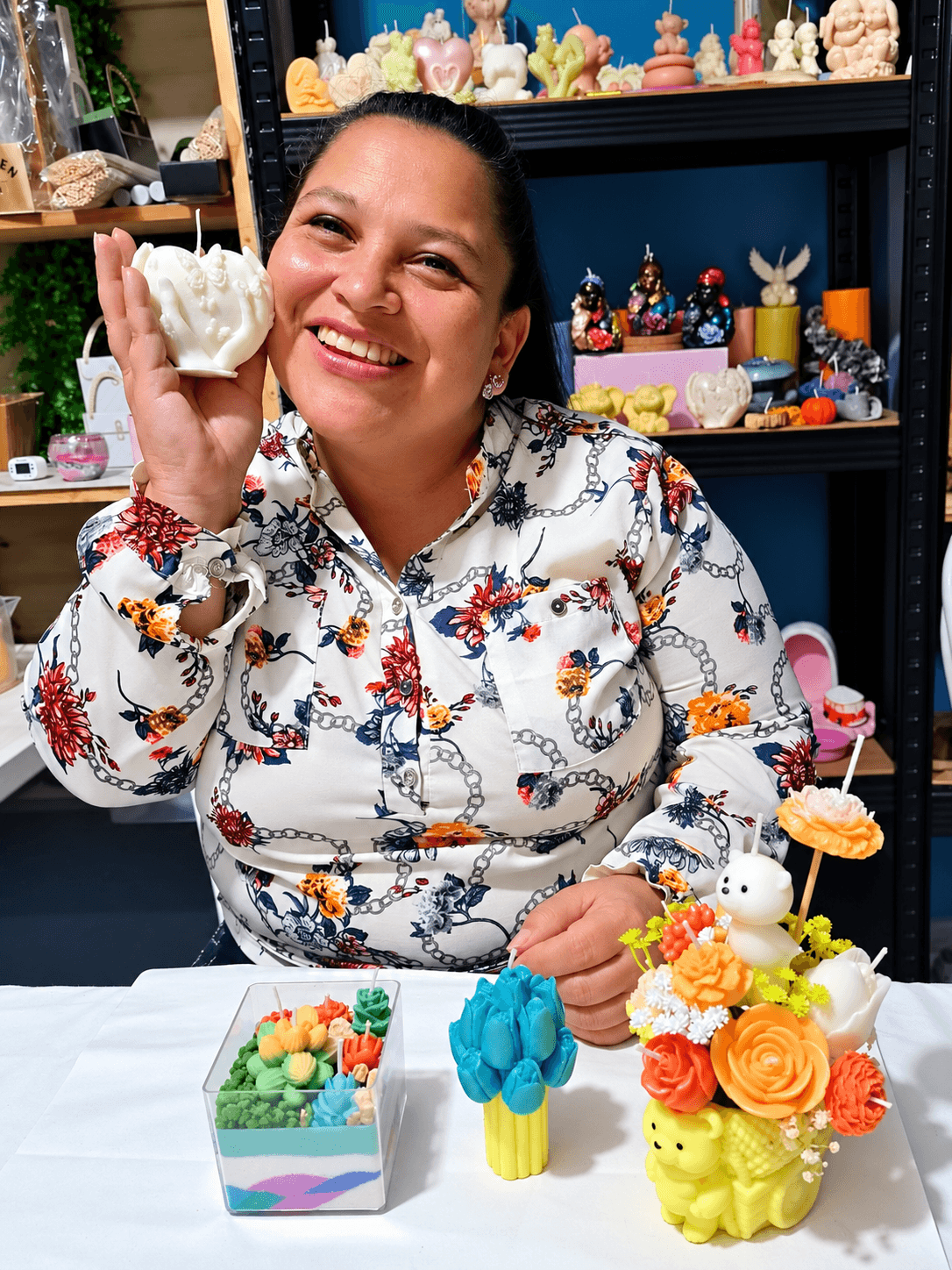 Participante mostrando una vela decorativa junto a sus arreglos en la mesa del taller