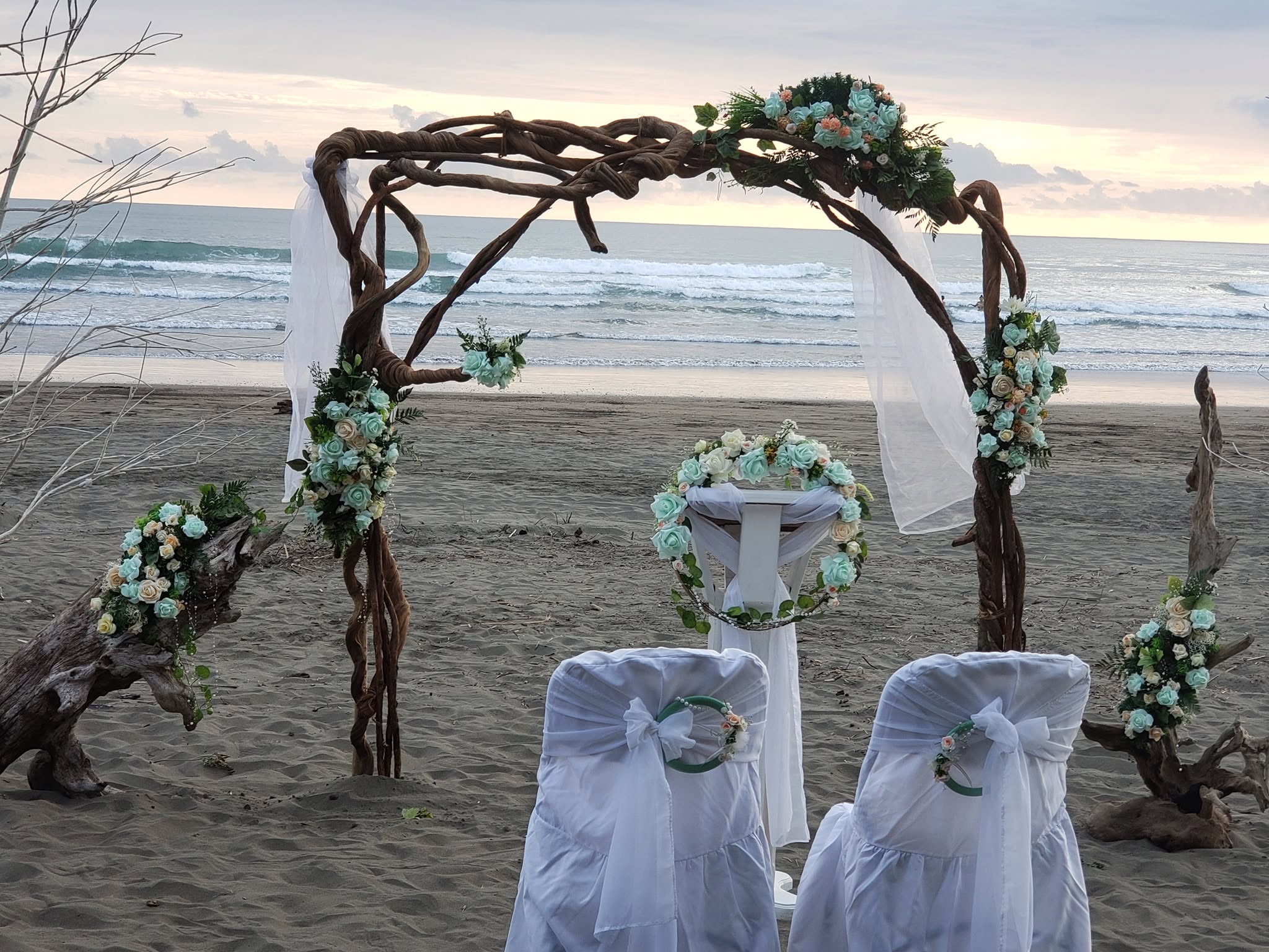 Arco de madera con flores blancas y sillas decoradas para una ceremonia frente al mar